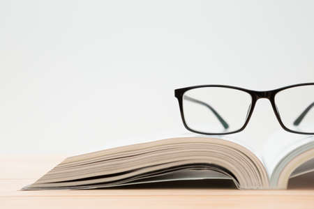 Glasses and open book on wooden table, white background and copy spaceの写真素材