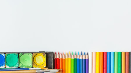 Top view of Colorful Watercolor palette, paintbrush, colored pencils and drawing equipment on white...