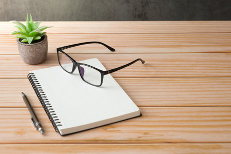 Notebooks, pens, glasses, cactus on wooden desks and loft walls with sunlight and copy space