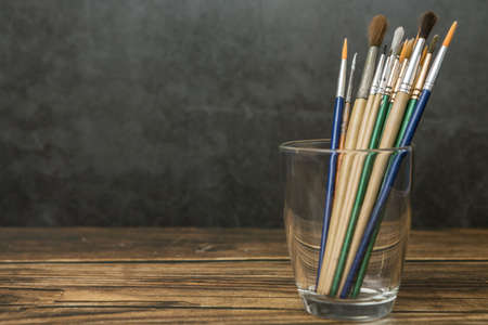 Many art brushes in the glass on a wooden and cement wall background and copy spaceの写真素材