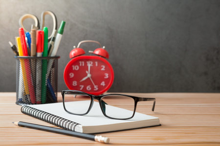Notebooks, pens, pencil holder, glasses, Red alarm clock on wooden desks and loft walls with...