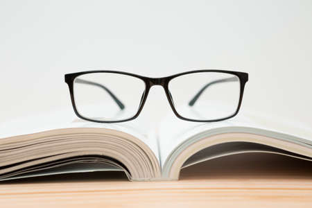 Glasses and open book on wooden table, white background and copy spaceの写真素材