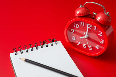 Notebook, pencil, red alarm clock on a red background and copy spaceの写真素材