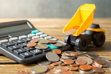 Dump truck, coins stack, calculator on wooden desks and loft walls with sunlight and copy space for money saving conceptの写真素材