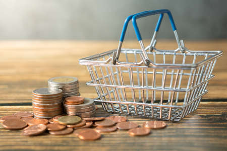 Shopping basket, coins stack on wooden desks and loft walls with sunlight and copy space for money saving conceptの写真素材