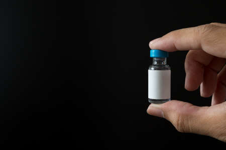 Hand holding vaccine bottles on black background for the concept and copy spaceの写真素材