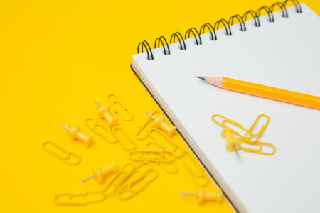 Selective focus of Notebook, pencil, clip and pin on a yellow background and copy space