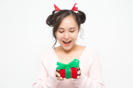 Beautiful Asian woman wearing small Santa hat and wearing pink sweater holding red gift box on white background. Cute Asian woman smiling and cheerful on Christmas and New Year's Day.の写真素材