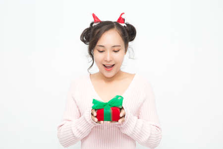 Beautiful Asian woman wearing small Santa hat and wearing pink sweater holding red gift box on white background. Cute Asian woman smiling and cheerful on Christmas and New Year's Day.の写真素材
