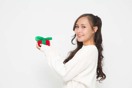 Beautiful Asian woman wearing white sweater holding red gift box on white background. Cute Asian woman smiling and cheerful on Christmas and New Year's Day.の写真素材