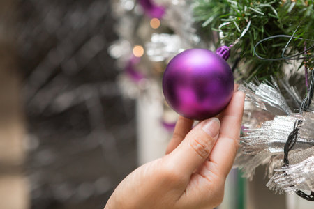 Hand holding Purple christmas ball on a Christmas tree decorated in Christmas and New Year's Dayの写真素材