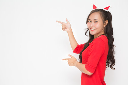 Beautiful Asian woman wearing small Santa hat and wearing red dress on white background. Cute Asian woman smiling and cheerful presenting something for Christmas and New Year's Day concept.の写真素材