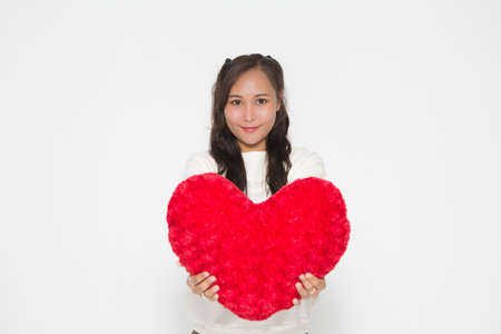 Beautiful Asian woman wearing white sweater holding red heart shape pillow on white background and copy space. Cute Asian woman smiling and cheerful for Valentine Day concept.の写真素材