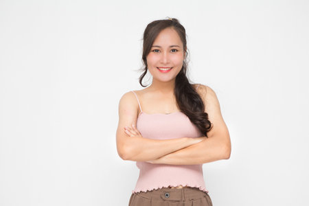 Beautiful Asian woman wearing pink casual shirt with her crossed arms on white background and copy space. Cute Asian woman smiling and cheerfulの写真素材