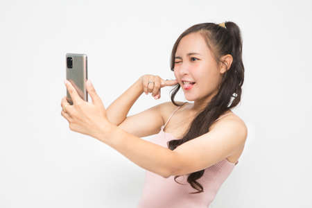 Beautiful Asian woman wearing pink casual shirt holding smartphone and selfie on white background and copy space. Cute Asian woman smiling and cheerful having fun selfies for social media conceptの写真素材