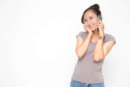 Beautiful Asian woman wearing grey casual shirt holding smartphone on white background and copy space. Cute Asian woman smiling and cheerful talk something on the phone for social media conceptの写真素材