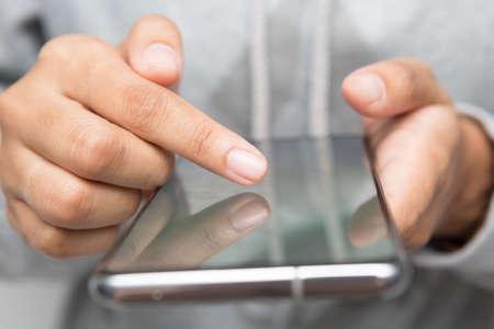 Close up of woman wearing grey casual shirt hand holding smartphone. Woman chatting about something for social media conceptの写真素材