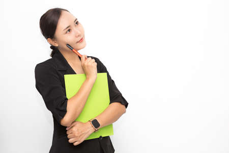 Beautiful Asian business woman wearing black suit holding document folder and pen and thinking something on white background and copy space. Confident Asian working woman smiling and cheerfulの写真素材