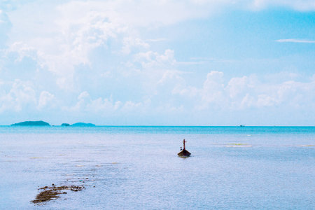 The beach has a small boat on it. Bright sky mountain background