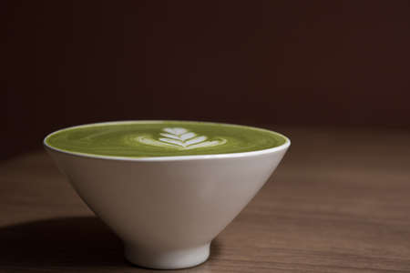 green tea latte in white ceramic cup on wooden table with brown backgroundの写真素材