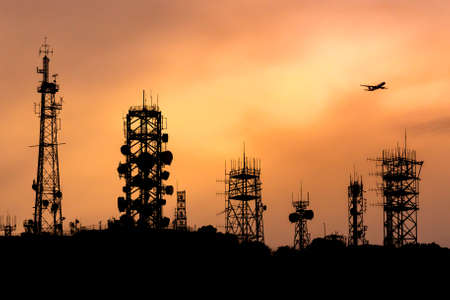 Silhouette  of communication towers  on mountain with airplane aboveの写真素材