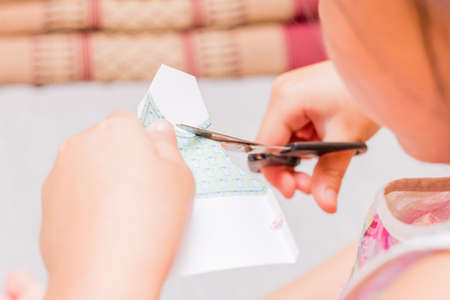 The little girl is cutting color paper. The little girl makes handcraft.の写真素材