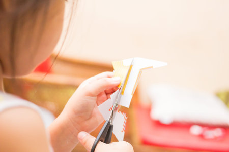 The little girl is cutting color paper. The little girl makes handcraft.