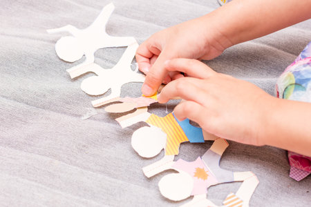 The little girl is gluing color paper. The little girl makes handcraft.