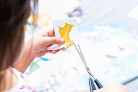 The little girl is cutting color paper. The little girl makes handcraft.の写真素材