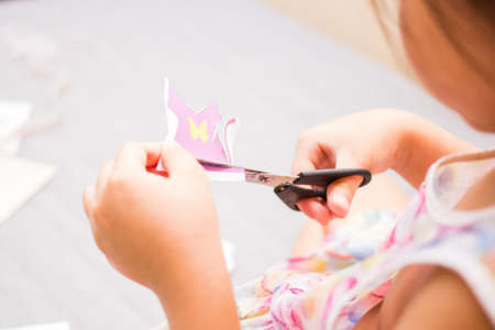 The little girl is cutting color paper. The little girl makes handcraft.の写真素材