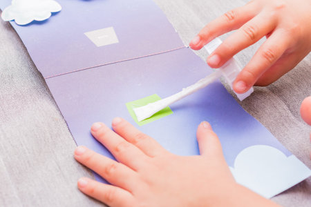 The little girl is gluing color paper. The little girl makes handcraft.