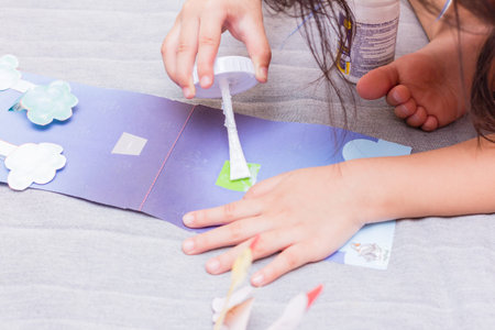 The little girl is gluing color paper. The little girl makes handcraft.