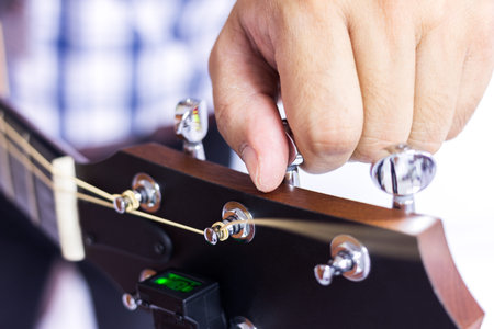 Person tuning a guitar over white background in selective focus