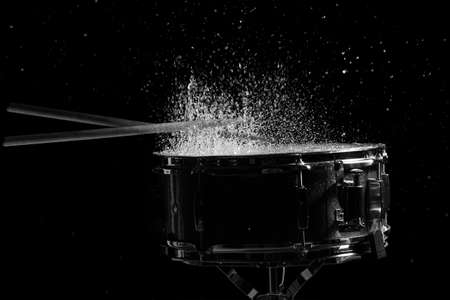 The drum sticks are hitting on the snare drum with splash water in low light backgroundの写真素材