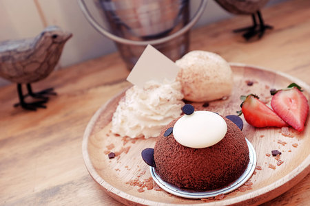 Cute and delicious brown bear cake served with strawberry, vanilla ice cream and whipped cream in wooden plate.Those are placed on the wooden table.Chocolate Mousse Cakesの写真素材