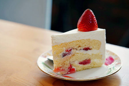 A strawberry shortcake topped with a large fresh strawberry placed in white plate and on wooden...