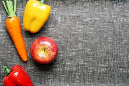 Top view with copy space. Fresh colorful Vegetables consists of orange carrot, red apple, Yellow and red bell pepper on gray textured background, ready for adding text or mockup.の写真素材