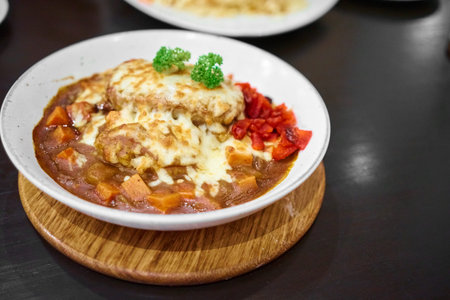 Delicious Japanese hamburg curry Serve with and mozzarella cheese on top with Rice, curry Rice in white plate on a black table with copy space.の写真素材