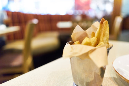 Junk food, French fries contained in stainless steel cup placed on a table. Restaurant scene...