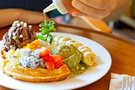 Dessert, waffles served with mixed fruits, sliced banana, chocolate ice-cream and green tea ice-cream and topped with white chocolate was pouring with honey.の写真素材