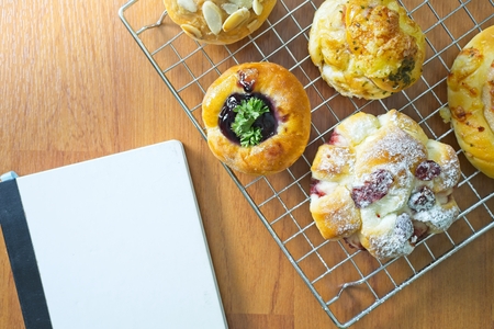 Top view and copy space, Freshly Baked danish pastry on wooden background, assorted bread and pastry, Different kinds of bread rolls. Kitchen or bakery poster design with notebookの写真素材