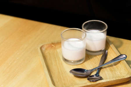 Panna cotta is an Italian dessert of sweetened cream thickened with gelatin and molded. two glasses of panna cotta dessert on wooden table with spoons.の写真素材