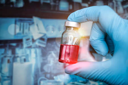 Doctor holding vaccine and the solution is red for prevention, immunity and treatment from covid-19 infection or coronavirus. Scientific and medical concepts. Focus on vaccine bottle , blurred background.の写真素材