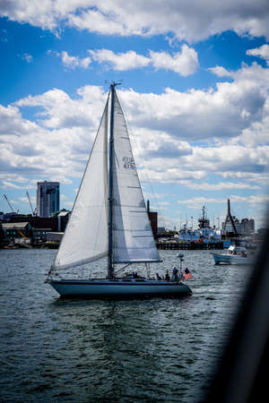 beautiful white sailboat at a busy bay with the sail open and ready to goの写真素材
