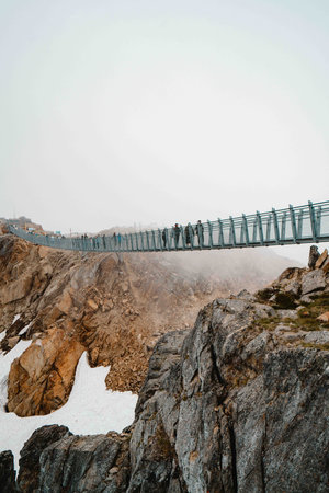 large suspension bridge connecting two mountain peaks during a foggy day in the winterの写真素材
