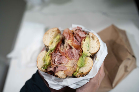 huge breakfast everything bagel stuffed with ingredients like ham cheese bacon and avocado