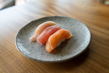 three colorful sushis at japanese restaurant on top of plate and wooden tableの写真素材