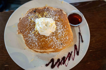 delicious breakfast pancakes with powdered sugar, whipped cream, and syrup on the side at brunch restaurantの写真素材