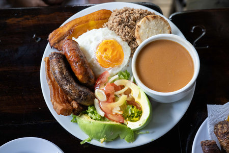 delicious bandeja paisa platter in medellin, colombia at restaurant for lunch. platter of salad, avocado, tomato, egg, rice, beans, blood sausage, chorizo, pork belly, plantain, arepa, and beefの写真素材