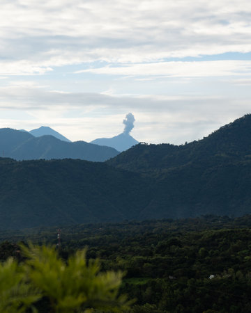 vertical capture of large volcano erupting in guatemalan countryside in central america during a cloudy dayの写真素材